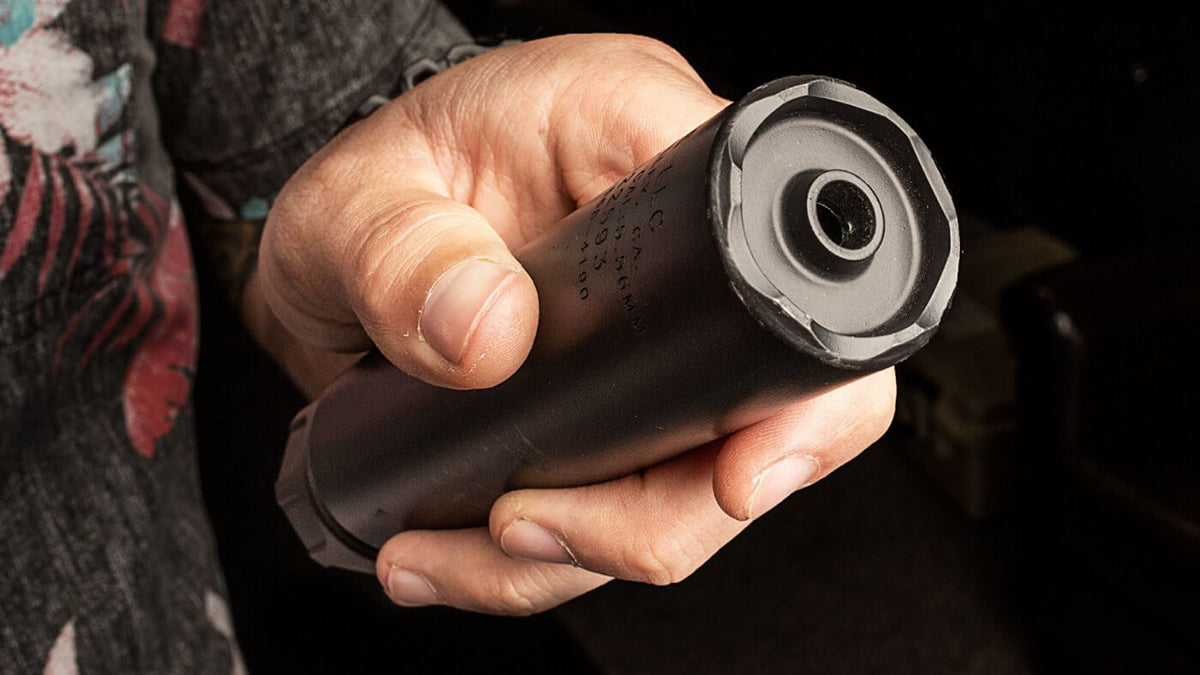 a person holds a black surefire suppressor in their hand, showing the front end