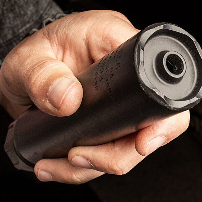 a person holds a black surefire suppressor in their hand, showing the front end