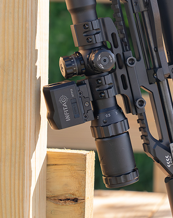 INFITAC ATP13 Thermal Reflex Sight mounted on an air rifle above a riflescope, displayed beside a wooden shooting rest, highlighting the compact thermal optic integrated into the rifle setup.