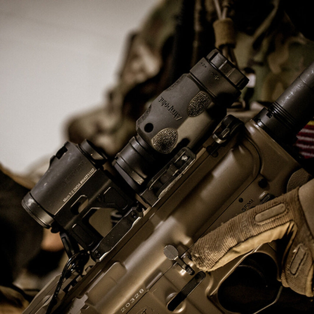 An operator with an AR15 setup, featuring an attached Aimpoint 3XMag-1 Magnifier and a Micro T2 sight.