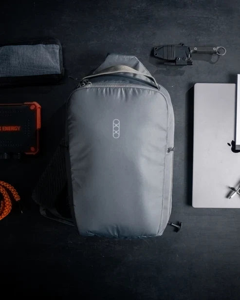 Flat lay of the Eberlestock Fade Sling XL in black surrounded by everyday carry gear, including a portable power bank, folding knife, laptop, and paracord, illustrating a full EDC loadout.