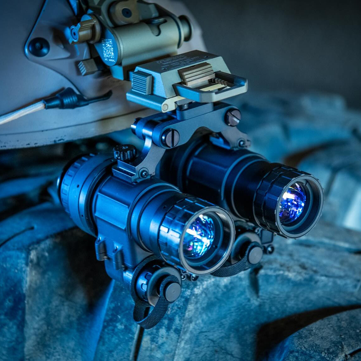 an image of a binoculars that is mounted on a helmet using a bridge mount and is rested on top of a metal surface seemingly set aside after being use or put up for display