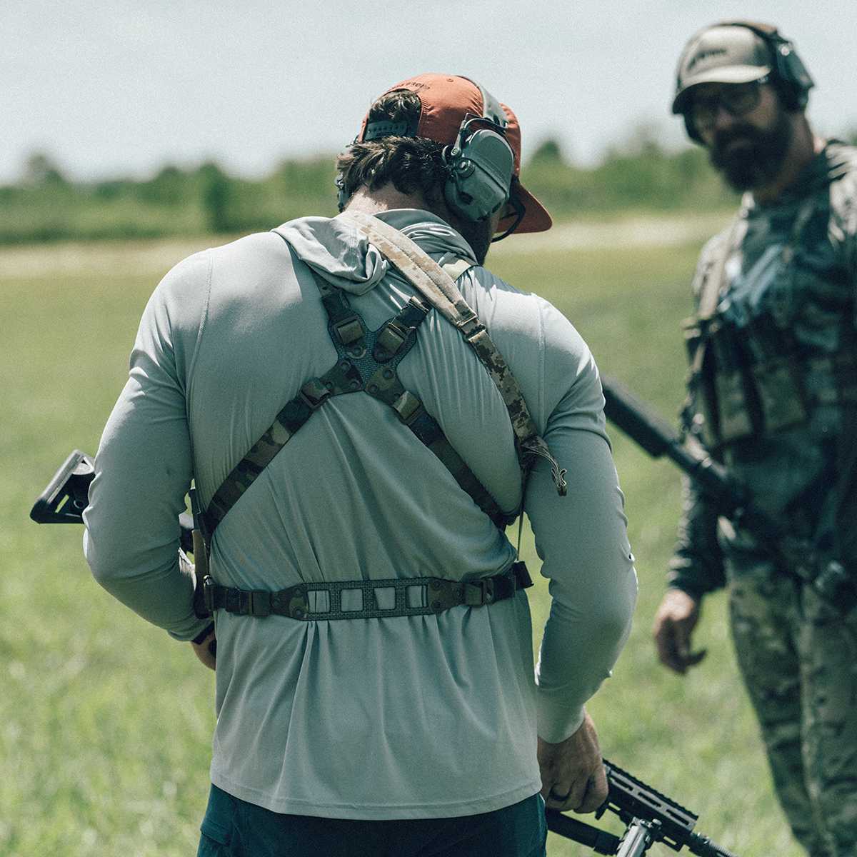 Two men that are out in the field and are wearing chest rigs and carrying guns 