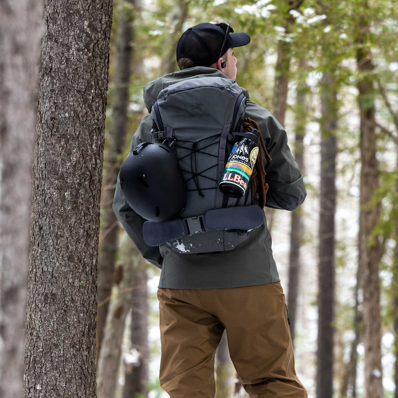 A hunter trekking through the backcountry wearing the Eberlestock Mainframe II Pack Frame in the Mountain colorway, fully loaded with a Vapor 2500 bag, a secured rifle, and a harvested trophy head on the meat shelf.