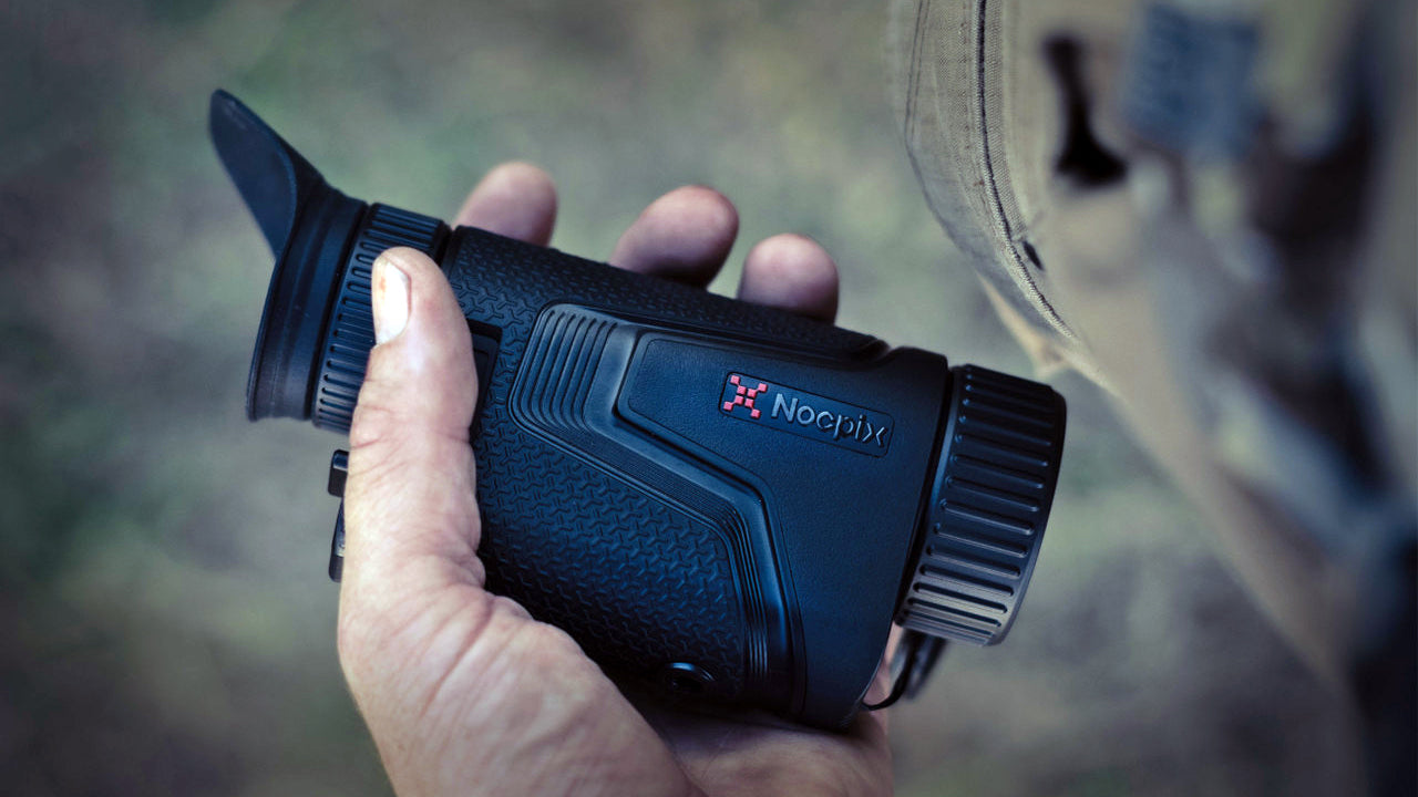 an image of the infiray nocpix handheld thermal in the color black and is in the color black where the item looks like it is being held by a military personnel while he is on the field. 
