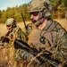 A profile view from the left side showing two maritime tactical operators crouching in a field while wearing the 3M Peltor ComTac IX ARC headset integrated with a rugged 3M Peltor FL7000 PTT and SecureFit 500 safety eyewear for reliable dual radio communication in the field.