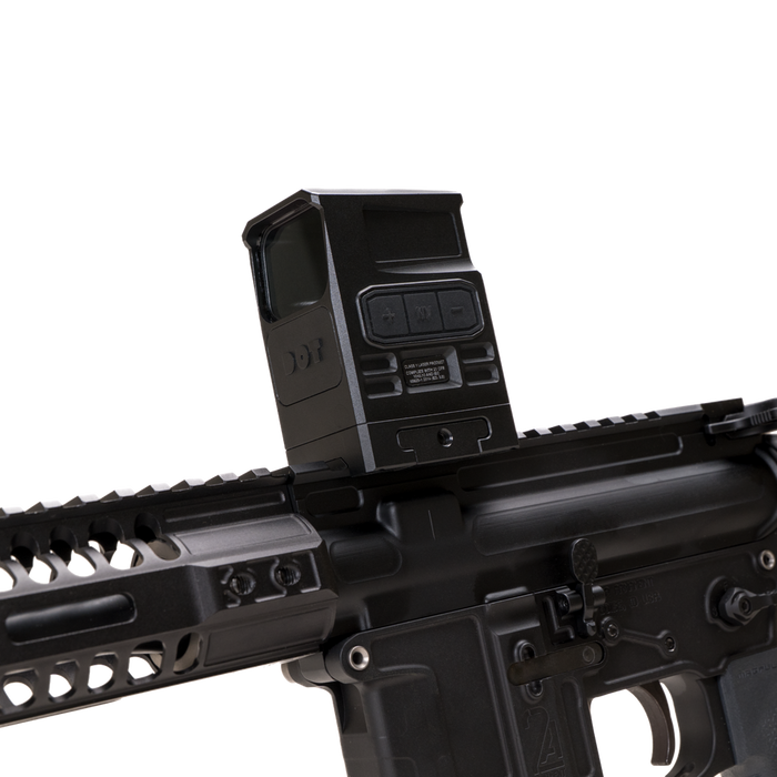 the image showcases the DOT EHS-1 L Holographic Sight in the color black and is being attached directly on a black rifle where the rifle is tilted slightly downwards and we can see the adjustment dials on the left side of the holographic sight. 