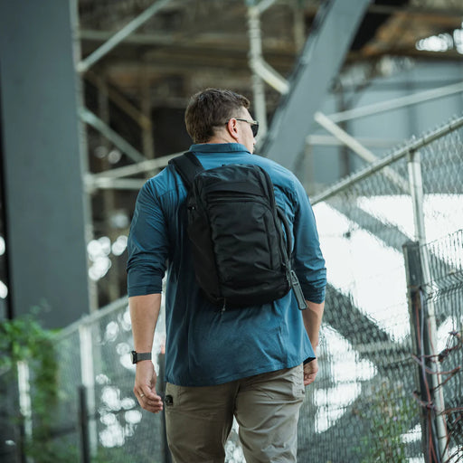An undercover officer blending into a crowd while wearing the black Gamut 18L Sling Bag, demonstrating the pack's ability to maintain a low-profile "grey man" appearance in public.