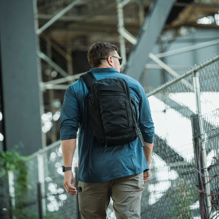 An undercover officer blending into a crowd while wearing the black Gamut 18L Sling Bag, demonstrating the pack's ability to maintain a low-profile "grey man" appearance in public.