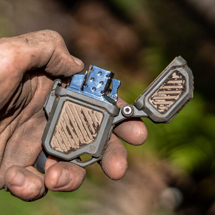 Camper using the Thyrm PyroVault 2.0 while his hands and the Zippo case are covered in dirt.