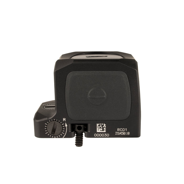 a side product photo of the Trijicon RCR Red Dot Sight against a plain white background and prominently featured at the front-left, reflecting a dramatic green and orange dichroic coating and showing small white laser-engraved markings are visible along the base on the side saying '000030', 'RC01', and 'ISA 58:8'. At the base-front, another adjustment dial and 'UP' text with directional arrows are visible, and a short portion of a black mounting screw extends from the rear
