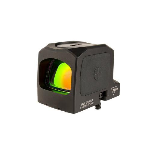 an isometric product photo of the Trijicon RCR Red Dot Sight against a plain white background and prominently featured at the front-left, reflecting a dramatic green and orange dichroic coating and showing small white laser-engraved markings are visible along the base on the right side: 'MADE IN USA PATENT PEND', with the small Trijicon 'Tri' triangle logo above it.
