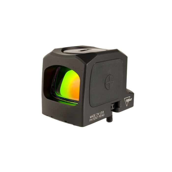 an isometric product photo of the Trijicon RCR Red Dot Sight against a plain white background and prominently featured at the front-left, reflecting a dramatic green and orange dichroic coating and showing small white laser-engraved markings are visible along the base on the right side: 'MADE IN USA PATENT PEND', with the small Trijicon 'Tri' triangle logo above it.
