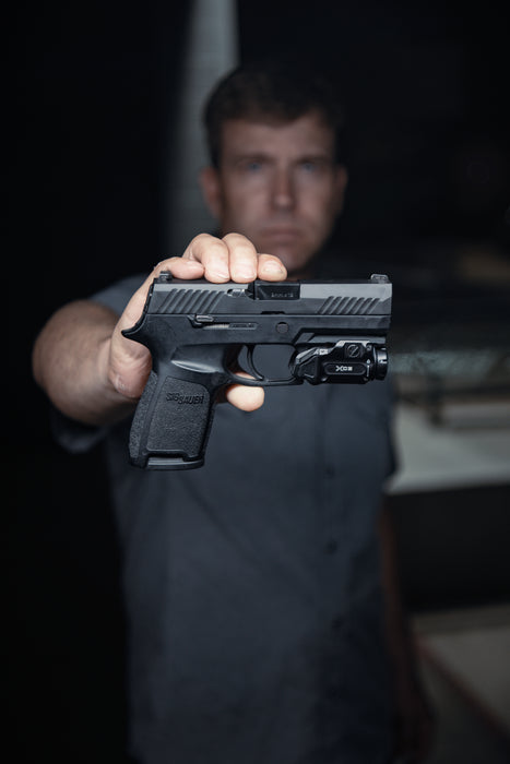 the xc3-b pistol weapon light that is attached on a black gun where the product model is holding the gun on it's side view and we can see how it is with the pistol light on it.
