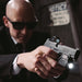 a bald person wearing sunglasses and a suit is holding a handgun with surefire xsc weaponlight attached, pointed towards the viewer