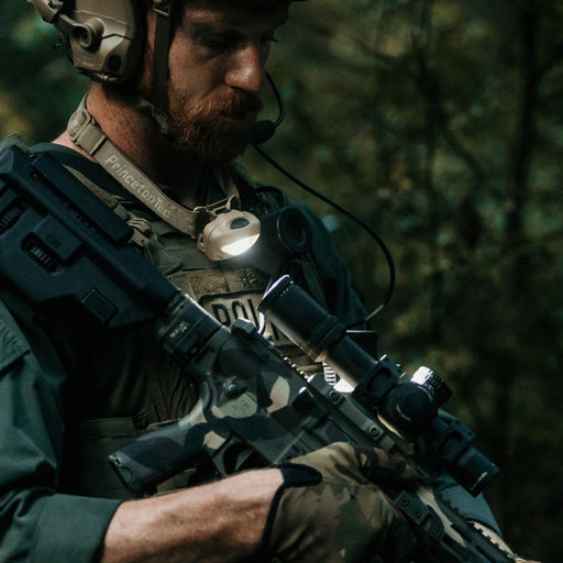 a bearded person wearing a princeton tec vizz 550 rgb and tactical gear holds a rifle and looks to the side