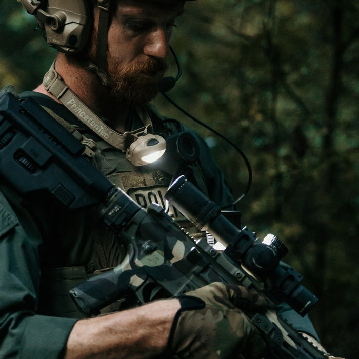 a bearded person wearing a princeton tec vizz 550 rgb and tactical gear holds a rifle and looks to the side