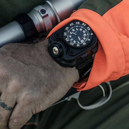 a close-up shows a person's hand wearing a surefire 2211 signature wristlight, resting on a firearm, with an orange sleeve visible in the background