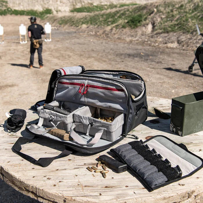 A fully opened cof heavy range bag rests on a shooting table at the range, clearly showing the spacious main compartment, the dedicated ammo section, and the removable magazine holder placed nearby.