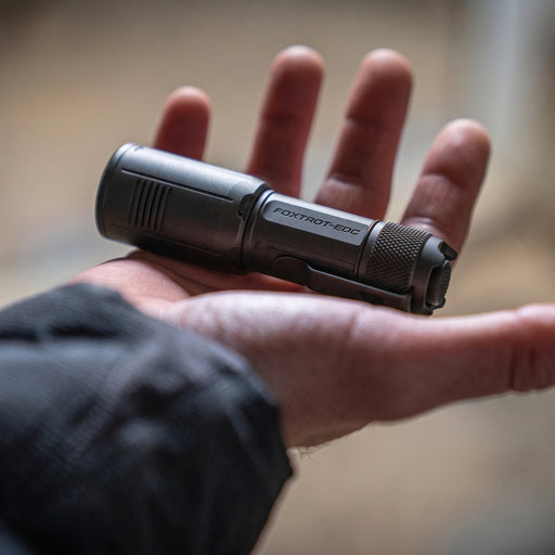A person holds the Foxtrot EDC Compact resting flat in the palm of their open hand, clearly demonstrating the small, easily concealable size of the flashlight.