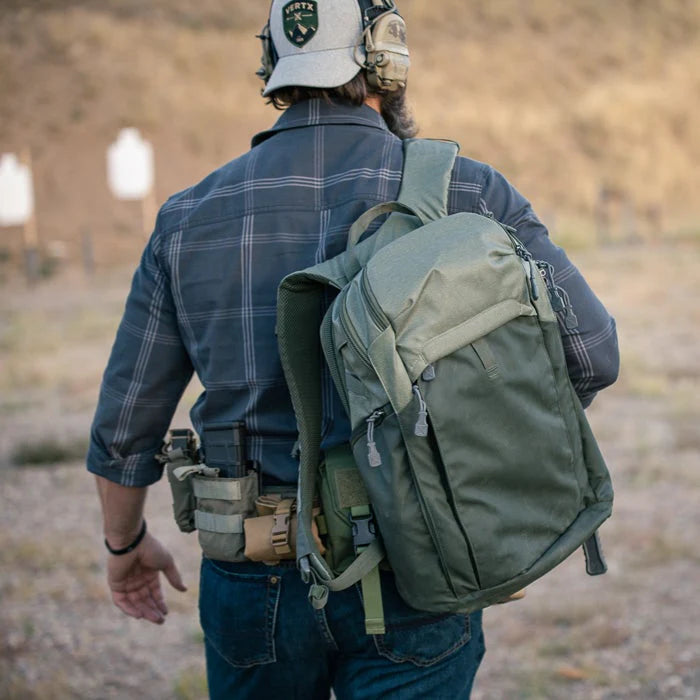 A shooter on the firing range wearing a Heather OD and Rudder Green Vertx Gamut CCW Tactical Backpack during training.