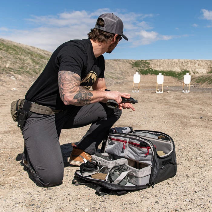 A shooter pulls a handgun from the padded sleeve of the cof heavy range bag , demonstrating the quick access provided by the large U-shaped top opening.