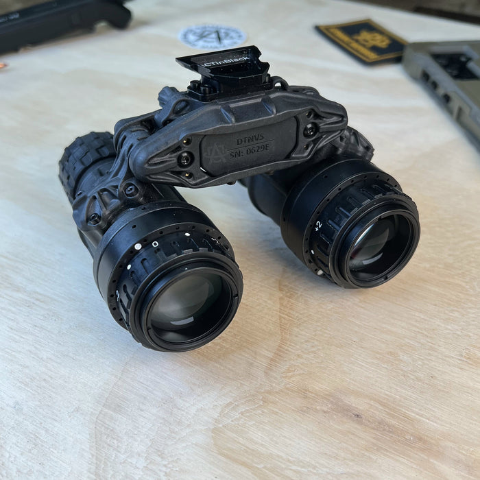 This rear-side angled view of the act in black dtnvs focuses on the high-performance objective lenses in the foreground, demonstrating the system's rugged dual-tube housing and the precision optics designed to provide a clear field of view in complete darkness. The perspective highlights the professional-grade construction and the individual monocular pods that enable tactical flexibility for elite operators.