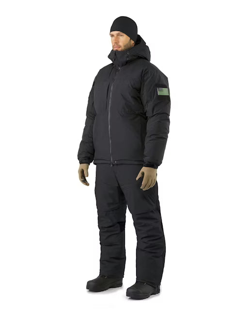 Full body side view of a person wearing the black Arcteryx wet weather jacket and matching insulated pants, featuring a tactical flag patch on the arm and a protective hood for severe storms.