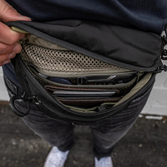 A top-down view inside the main compartment of the black Eberlestock Bando, revealing the mesh interior pocket organized with a wallet, keys, and sunglasses to showcase its generous capacity.