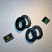 Two pairs of black oval gel earcup replacement seals for a ballistic headset are arranged on a textured tan surface alongside a holographic Atomic Defense sticker.