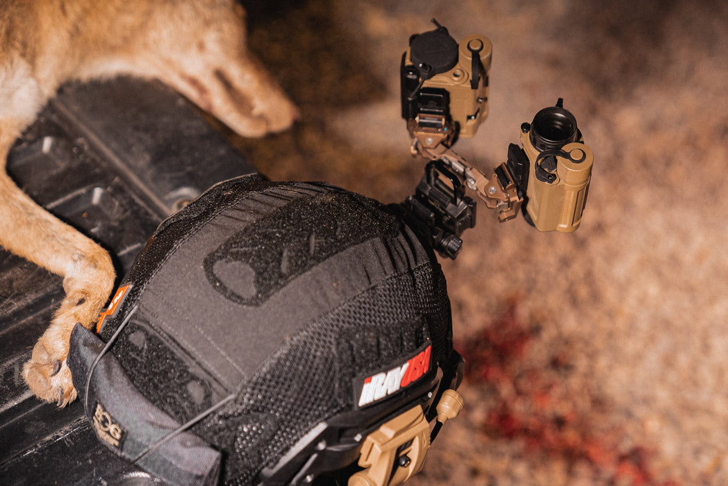 A black Team Wendy Exfil SL helmet sits on a truck bed, equipped with a dual-bridge setup featuring a standard night vision monocular paired with a rico micro rh25 v2 thermal device, placed alongside a recently hunted coyote.