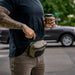 A bystander sipping coffee while effortlessly pulling his phone from the coyote brown bando bag eberlestock model, demonstrating its utility as a convenient everyday carry solution in public spaces.