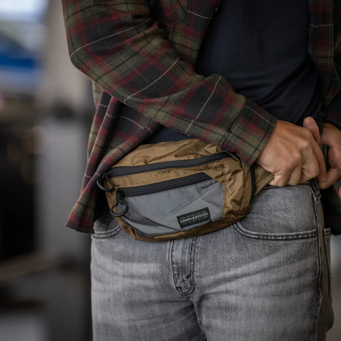A civilian disconnecting the main buckle on the Coyote Brown carrier, highlighting the durable hardware used to secure the bando bag extension strap during daily wear.
