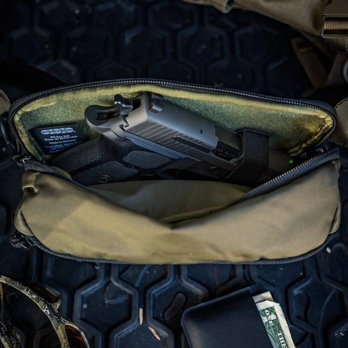 A close-up view looking into the rear pocket where a Glock 19 is securely positioned, effectively demonstrating the specific design features of the Eberlestock Bando Bag concealed carry compartment.