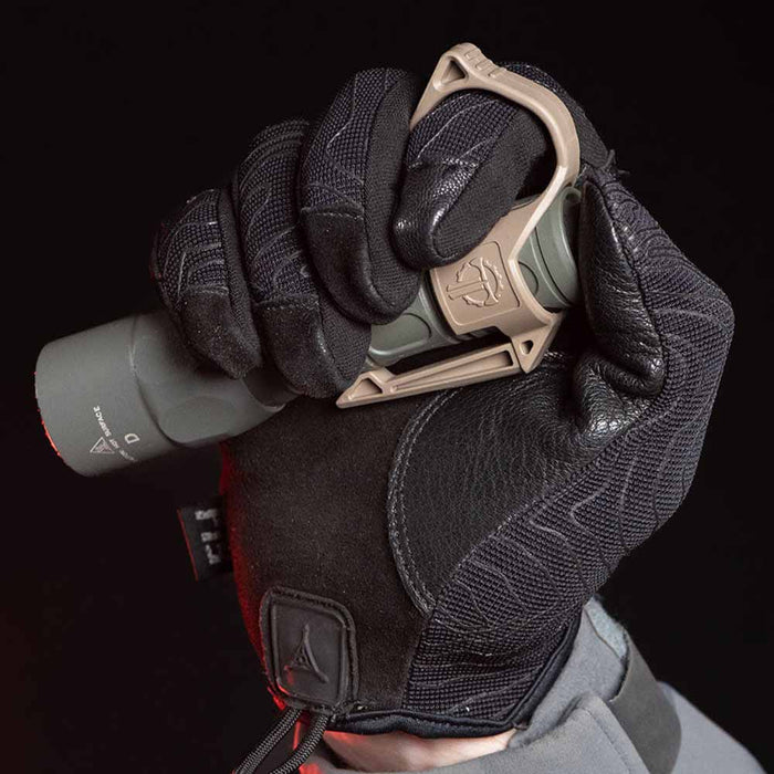 Close-up of a gloved hand holding a grey SureFire flashlight with a tan SwitchBack ring.