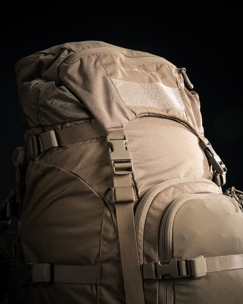 A detailed close-up shot of the high-capacity lid on the Eberlestock Brute 6500 105L Expedition Hunting Pack, showing the rugged zippers and weather-resistant fabric designed to protect small gear and electronics.