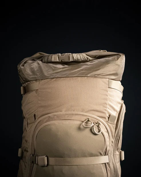 A detailed close-up shot of the Brute 6500 105L Expedition Rucksack shows the integrated roll-top expansion sleeve, which allows hunters to increase or decrease the bag's volume based on their gear needs.