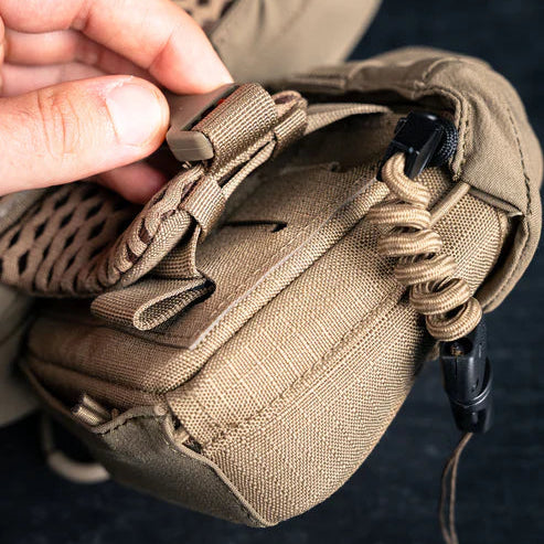 Close-up shot of the Eberlestock Bravo Mag-Free Rangefinder Pouch in Coyote Brown, featuring its MOLLE back and lanyard attachment in the foreground.
