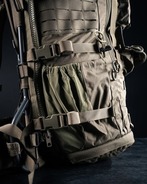A close-up view of the side profile on the green Eberlestock Military 5 Day Pack, focusing on the adjustable compression strap and a stretch-woven water bottle pocket in the foreground.