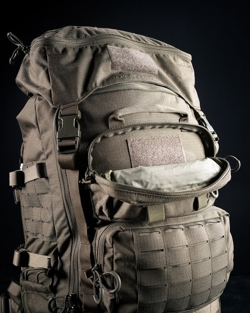 A detailed close-up of the upper front storage pouch on the exterior of the green Eberlestock Mission Ruck, highlighting its rugged material and accessible zipper compartment.