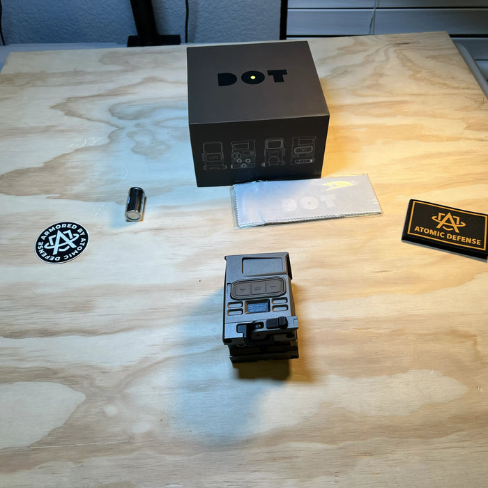 the dot ehs 1 holographic sight that is taken out of its box and is placed on top of a wooden table and is  presented on its right side view where there are also atomic defense pouches around it on the table