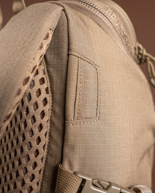 A precise close-up shot of the Eberlestock Brute Scout 30L Daypack showing the dedicated hydration port for a water bladder tube, with the ventilated air-mesh padding visible in the background to highlight the pack's heat-management features.
