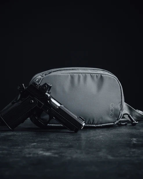 an image of the eberlestock fade flex micro in the color black and is presented with what looks to be a black pistol right beside it where all items are placed  in the center and on a black marble floor.