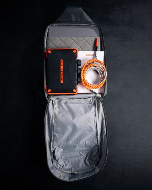 Overhead view of the Eberlestock Fade Sling XL fully open and packed with a laptop, notebook, portable power bank, and paracord bracelet, showing its everyday carry capacity.