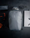Flat lay of the Eberlestock Fade Sling XL in black surrounded by everyday carry gear, including a portable power bank, folding knife, laptop, and paracord, illustrating a full EDC loadout.