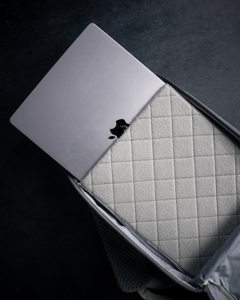 Close-up of the Eberlestock Fade Sling XL's padded laptop sleeve with a MacBook fitted inside, showing the quilted lining that protects electronics.