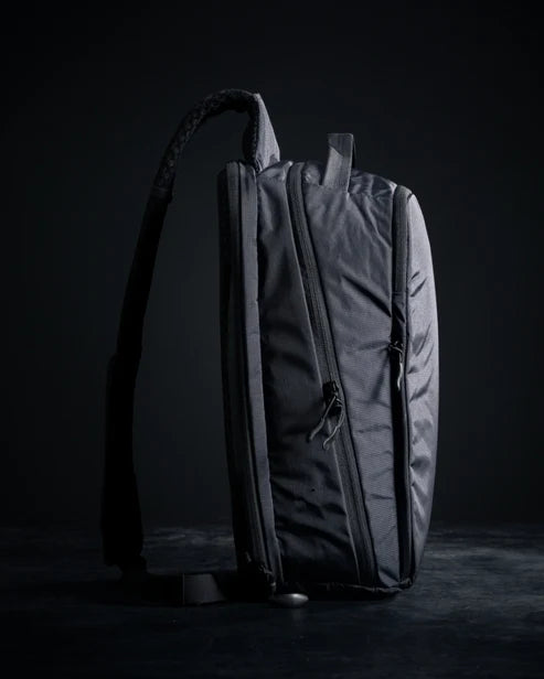 Side profile of the Eberlestock Fade Sling XL in black, showing the slim pack depth, top zipper pull, and adjustable sling strap with cam buckle.
