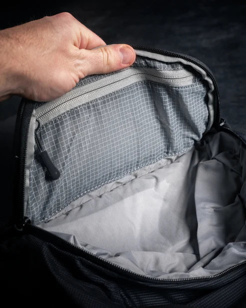 Close-up of a hand opening the top stash pocket on the Eberlestock Fade Sling XL, revealing the translucent mesh interior pocket for small valuables.
