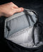 Close-up of a hand opening the top stash pocket on the Eberlestock Fade Sling XL, revealing the translucent mesh interior pocket for small valuables.