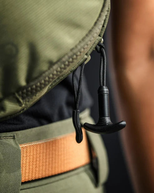 the image showcases the eberlestock fade flex micro in its olive variant and this image showcases the T-puller zipper feature that is danggling or attached on one zipper of the product and is dangling down